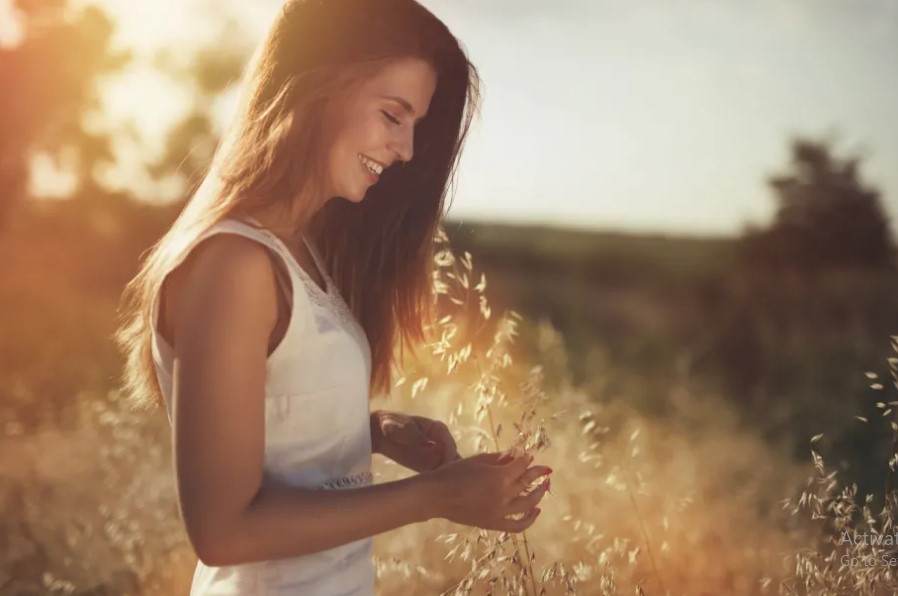 A woman stands gracefully in a lush green field, surrounded by tall grass under a clear blue sky.